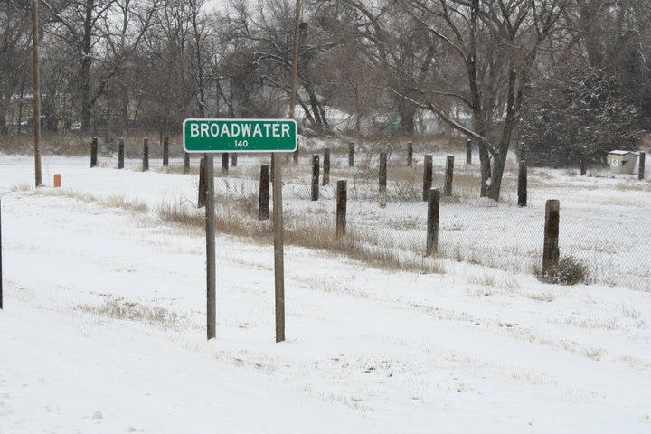 A snow-covered landscape features a green sign reading